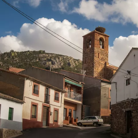 Calle del casco urbano de Fontanarejo (Ciudad Real) con la torre de la iglesia parroquial y sierras al fondo.