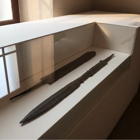 Vitrina baja con dos hojas antiguas, iluminadas por luz suave junto a una ventana.