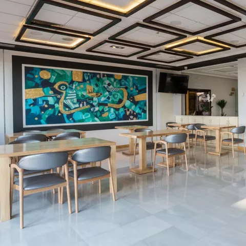 Salón amplio y moderno con mesas, sillas y una pintura decorativa en la pared.