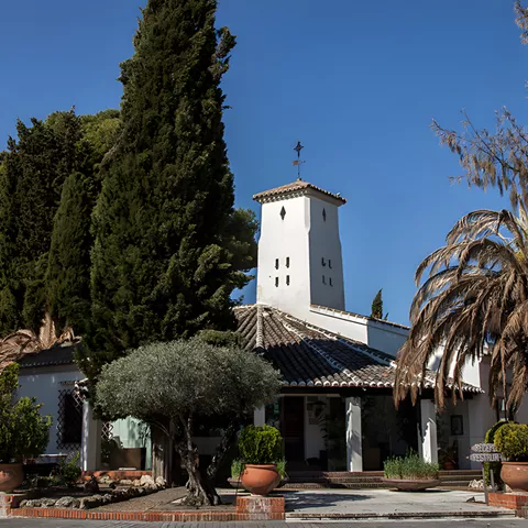 Edificio encalado rodeado de cipreses y palmeras