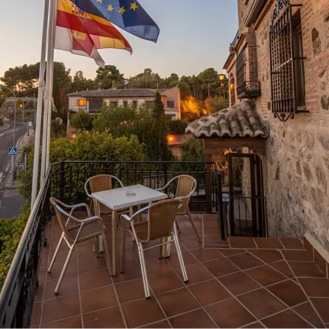 Terraza con mesa y sillas junto a banderas en un balcón al anochecer.
