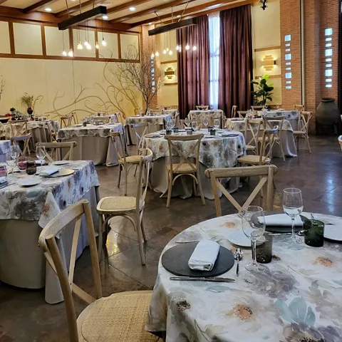 Comedor elegante con mesas redondas vestidas y techos de vigas de madera.