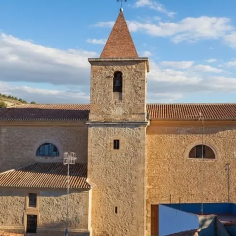 Iglesia de piedra de Hoya Gonzalo con torre campanario y tejado rojizo, situada junto al casco urbano.