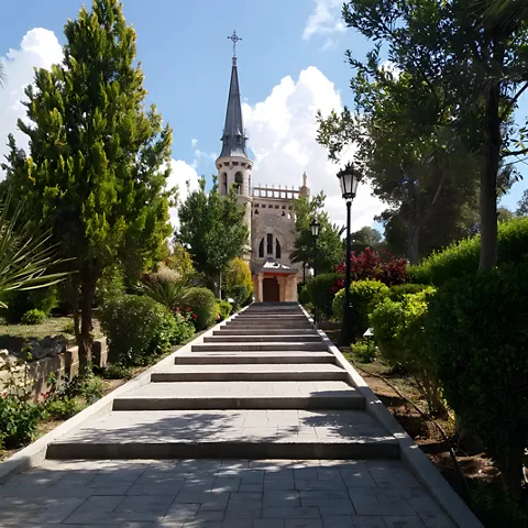 Escalinata entre jardines hacia iglesia con aguja