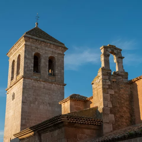 Detalle del campanario y espadaña de piedra sobre tejados de teja.