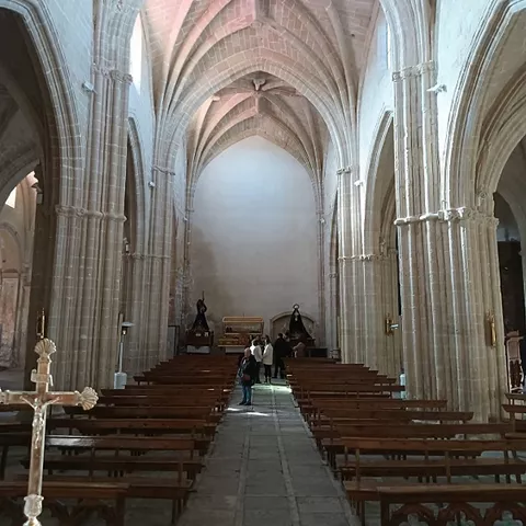 Interior de templo con nave central, bóvedas de crucería y bancos de madera.