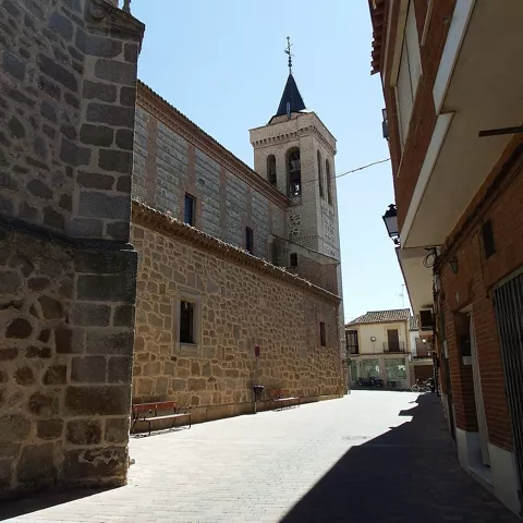 Calle estrecha junto a edificio religioso de piedra con torre campanario