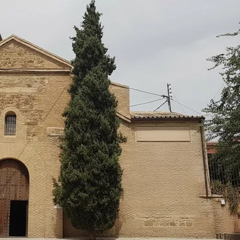 Fachada sencilla de ladrillo flanqueada por dos cipreses.