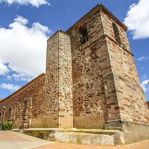Vista de una iglesia de ladrillos y piedras vistas sobre cielo claro con algunas nubes