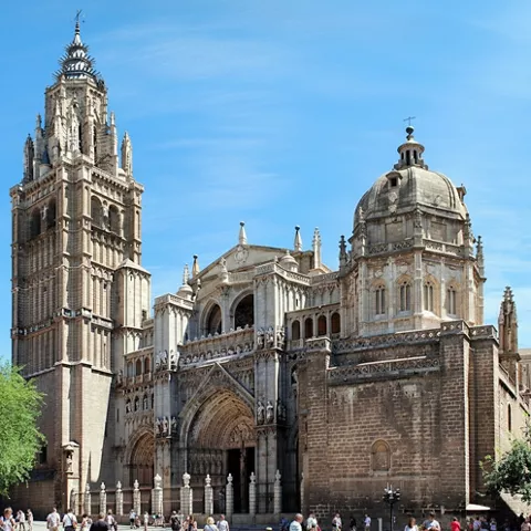 Catedral gótica con torre alta y cúpula junto a plaza concurrida.