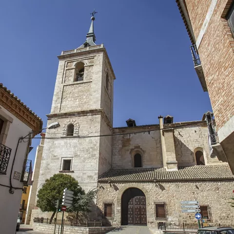 Iglesia de piedra con torre entre calles estrechas.