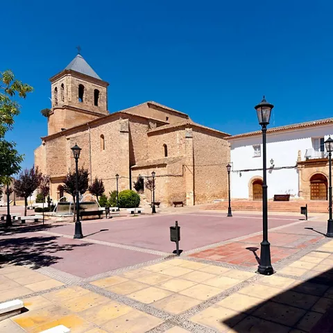 Iglesia de piedra vista desde una plaza con farolas y bancos
