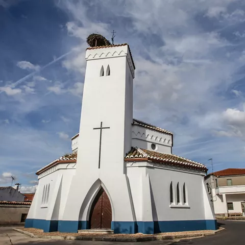 Iglesia blanca con torre y cruz en una calle del pueblo.