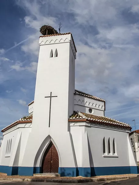 Iglesia blanca con torre y cruz en una calle del pueblo.