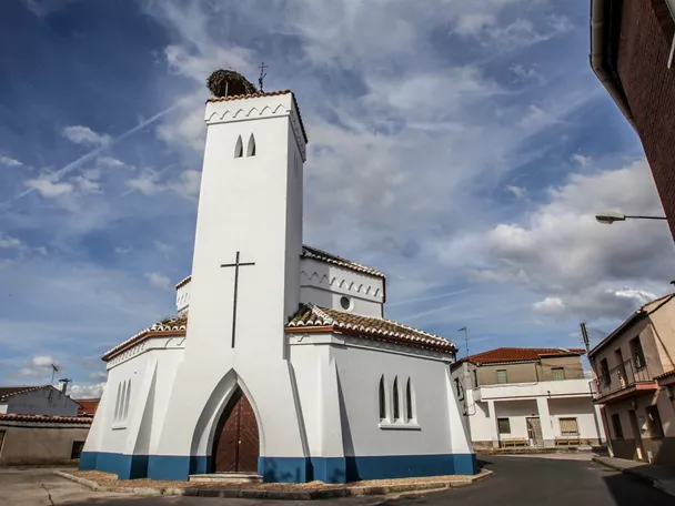 Iglesia blanca con torre y cruz en una calle del pueblo.
