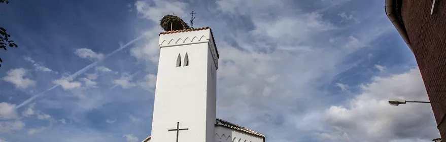 Iglesia blanca con torre y cruz en una calle del pueblo.