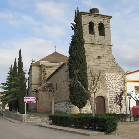 Iglesia de piedra con torre campanario junto a una plaza urbana