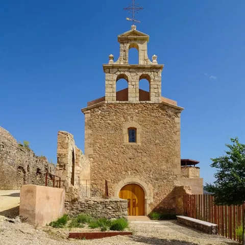 Iglesia de piedra con espadaña y puerta de madera en entorno rural.