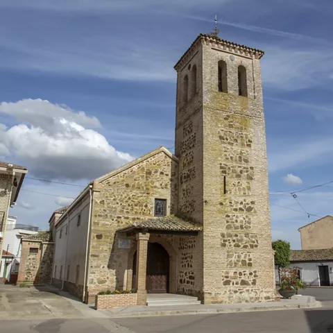 Iglesia de piedra con torre campanario en una plaza del pueblo.