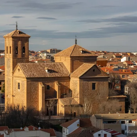 Iglesia de estilo tradicional destacando entre el casco urbano al atardecer.