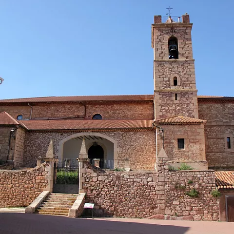 Iglesia de piedra con torre campanario y entrada elevada frente a una plaza.