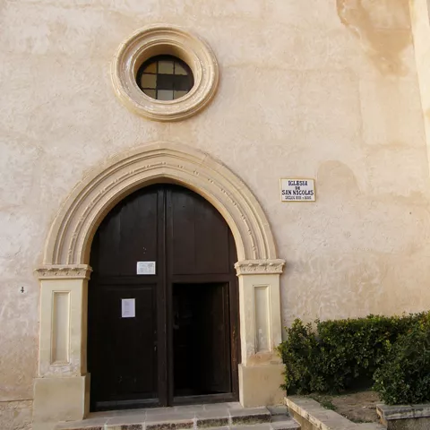 Puerta principal con óculo circular y farol en muro claro.