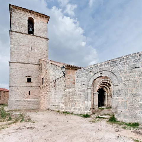 Conjunto de piedra con torre y arco románico en un entorno rural.