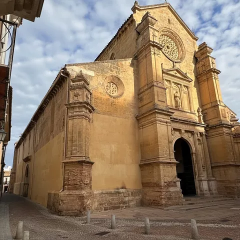Fachada lateral de iglesia de piedra con portada monumental y rosetón circular.