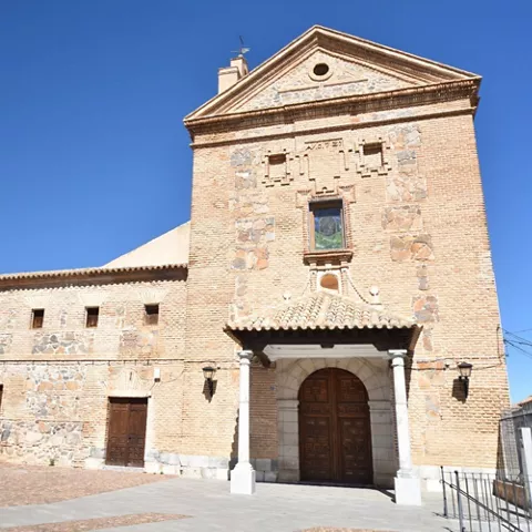 Fachada de edificio histórico de ladrillo y piedra con portada cubierta por tejadillo y columnas de piedra.