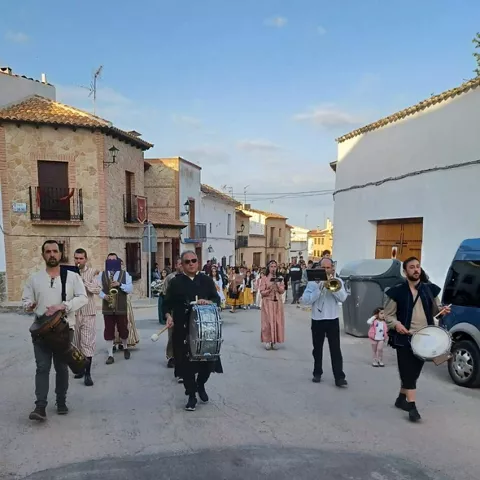 Desfile festivo con músicos y personas vestidas con trajes tradicionales por una calle del pueblo.