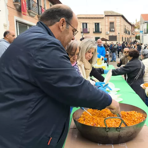 Reparto de comida en la plaza durante una jornada festiva con vecinos haciendo fila.