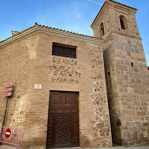 Fachada de iglesia de ladrillo y piedra con campanario y puerta de madera.