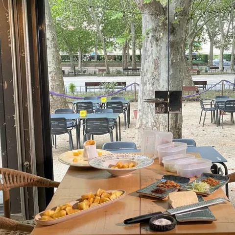 Mesa con tapas y platos frente a una terraza exterior con mesas vacías.