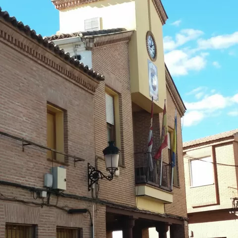 Ayuntamiento de ladrillo con reloj y balcón con banderas