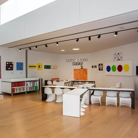 Espacio expositivo con obras geométricas y mesas.