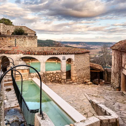 Lavadero tradicional de piedra con pilas de agua y vistas al paisaje rural.