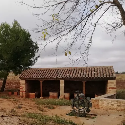 Lavaderos tradicionales de piedra junto a un campo rural y árboles.