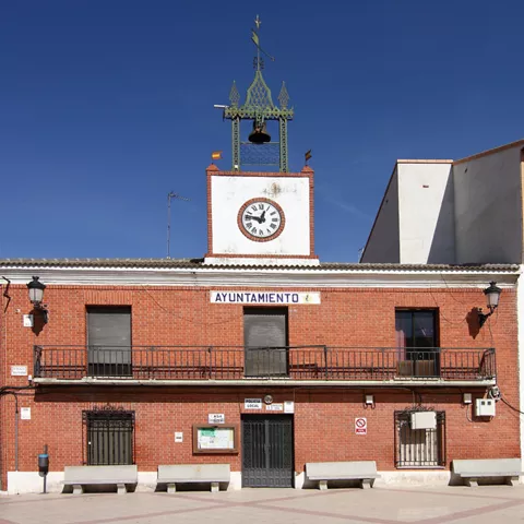 Fachada de ayuntamiento de ladrillo con reloj y campana