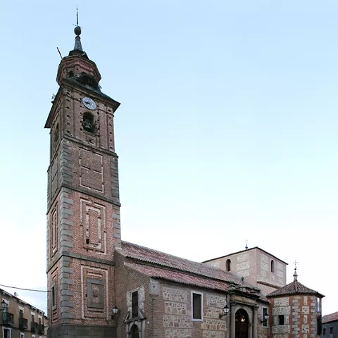 Iglesia de piedra con alta torre campanario y plaza