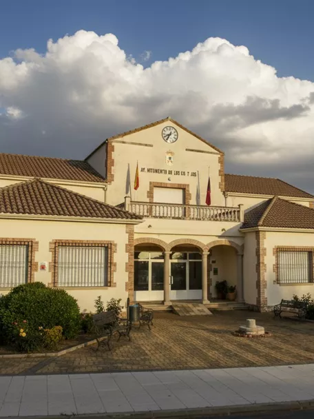 Fachada del Ayuntamiento de Los Cortijos (Ciudad Real) con plaza ajardinada y acceso porticado.