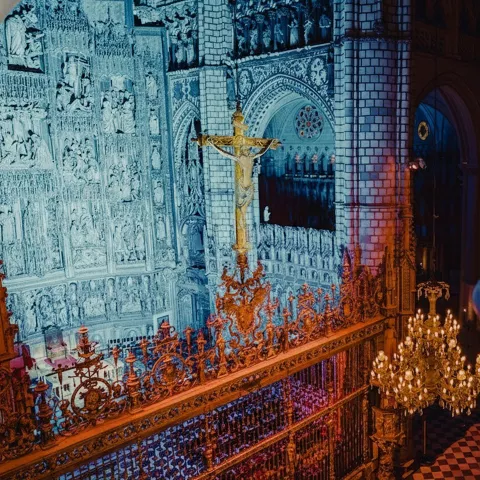 Crucifijo y rejería dorada con iluminación azul y lámpara de araña.