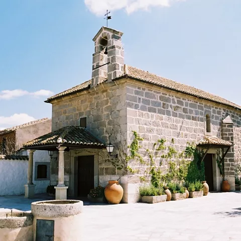 Ermita de piedra con pequeño campanario y patio soleado