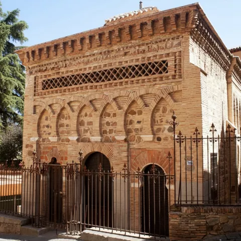 Vista exterior de edificio de ladrillo con arcos y reja de hierro.
