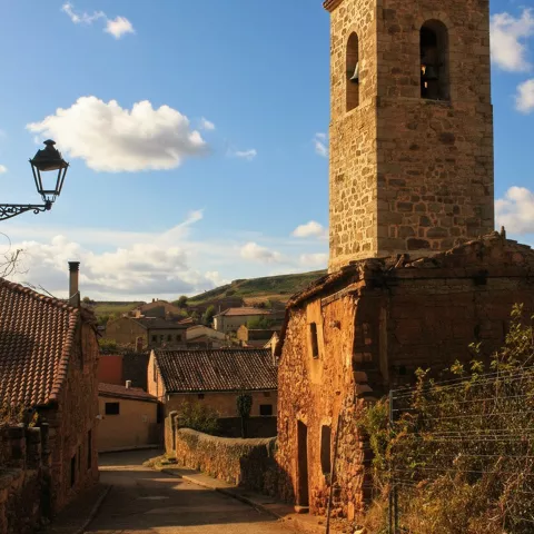 Torre de iglesia de piedra sobresaliendo entre casas tradicionales.