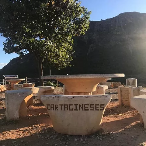 Zona de descanso con mesas y bancos de piedra junto a un mirador.