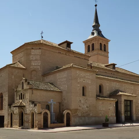 Iglesia de ladrillo y piedra con torre puntiaguda en una plaza