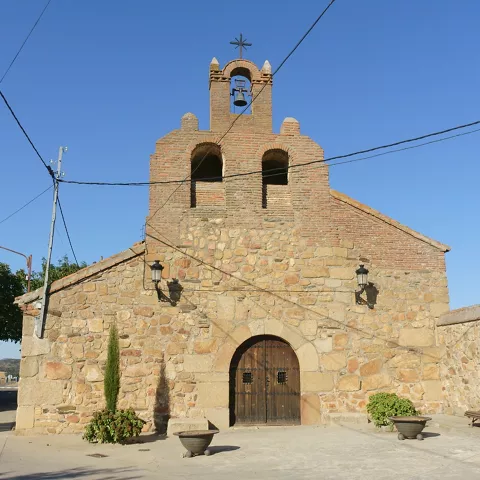 Ermita de piedra con espadaña, banco y macetas en la entrada