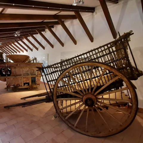 Sala interior con maquinaria agrícola antigua y carro de madera