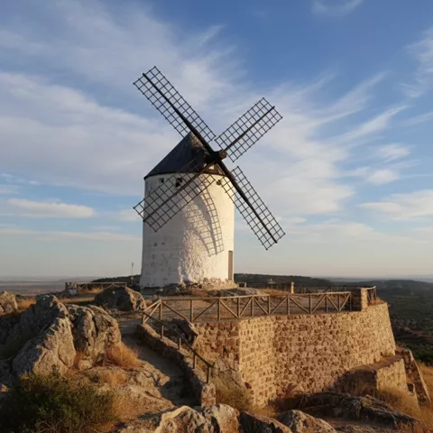 Molino de viento sobre plataforma de piedra en un promontorio rocoso, con llanura al horizonte.