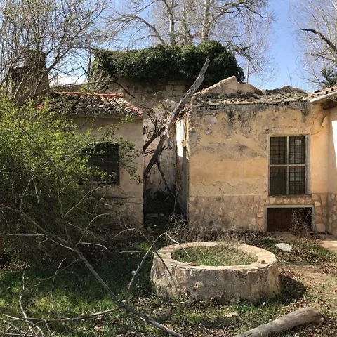 Conjunto de edificaciones antiguas con pozo circular en un entorno abandonado.